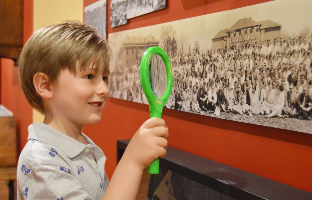 A boy looks through a magnifying glass at the Cookeville History Museum.